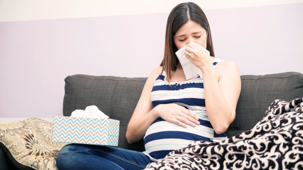 a woman blowing her nose because she the flu during pregnancy
