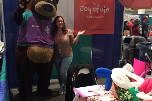 A surrogate mom taking picture with a big teddy bear - Joy of Life Surrogacy