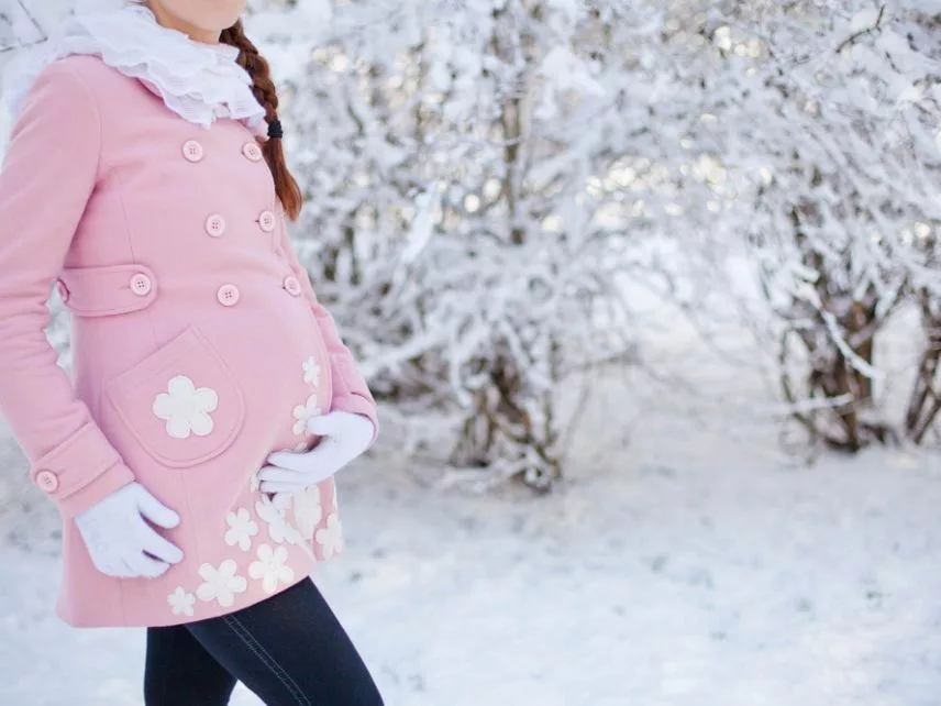 A pregnant mom wearing pink coat and walking on the snow road - Joy of Life Surrogacy