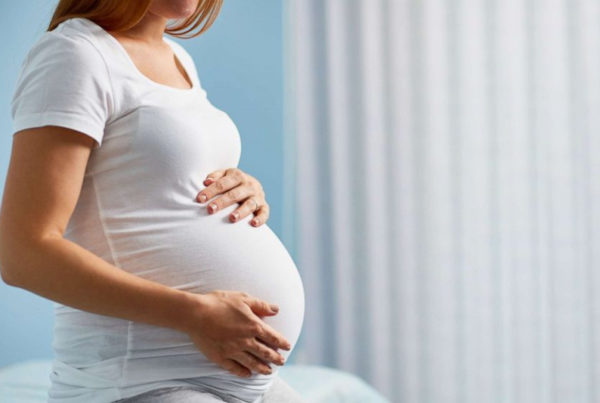 一位怀孕的妈妈穿着白色 T 恤坐在床上 - Joy of Life Surrogacy