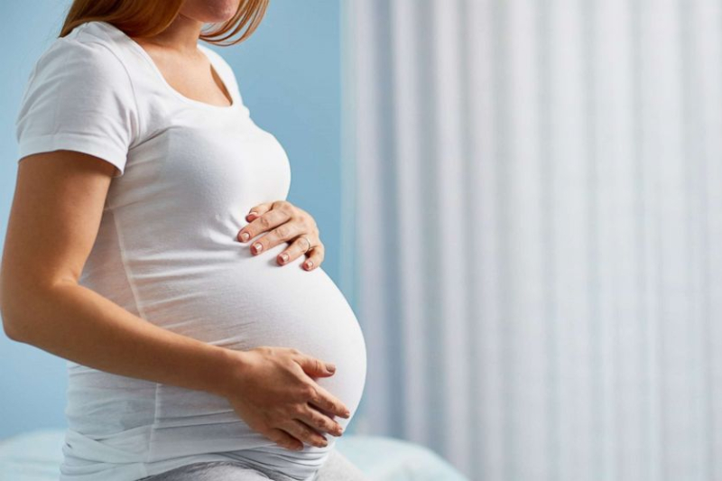 A dressed pregnant woman was setting on the bed - Joy of Life Surrogacy