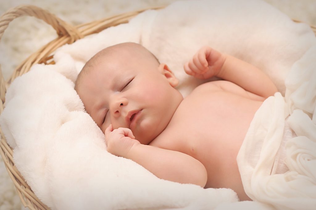 a newborn baby lying on a wood baby cradle - Joy of Life Surrogacy