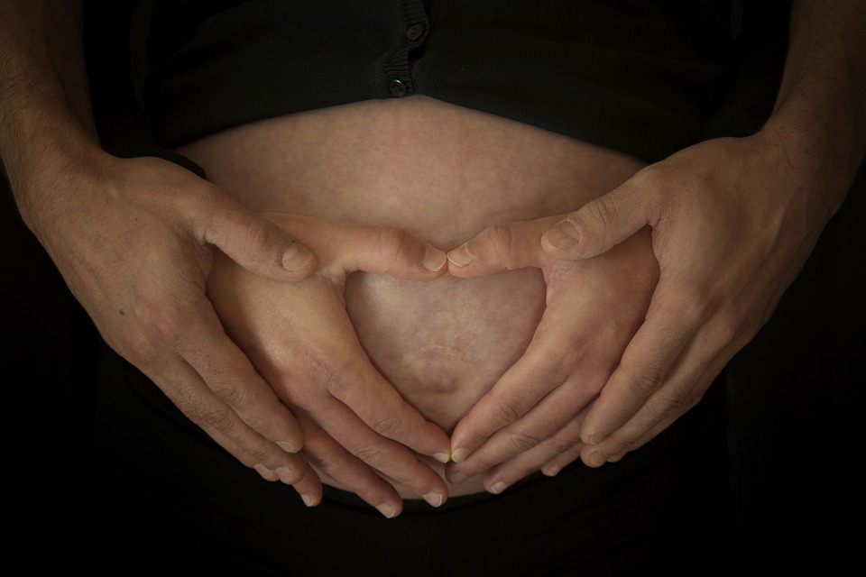 4 hands on pregnant mom's belly - Joy of Life Surrogacy